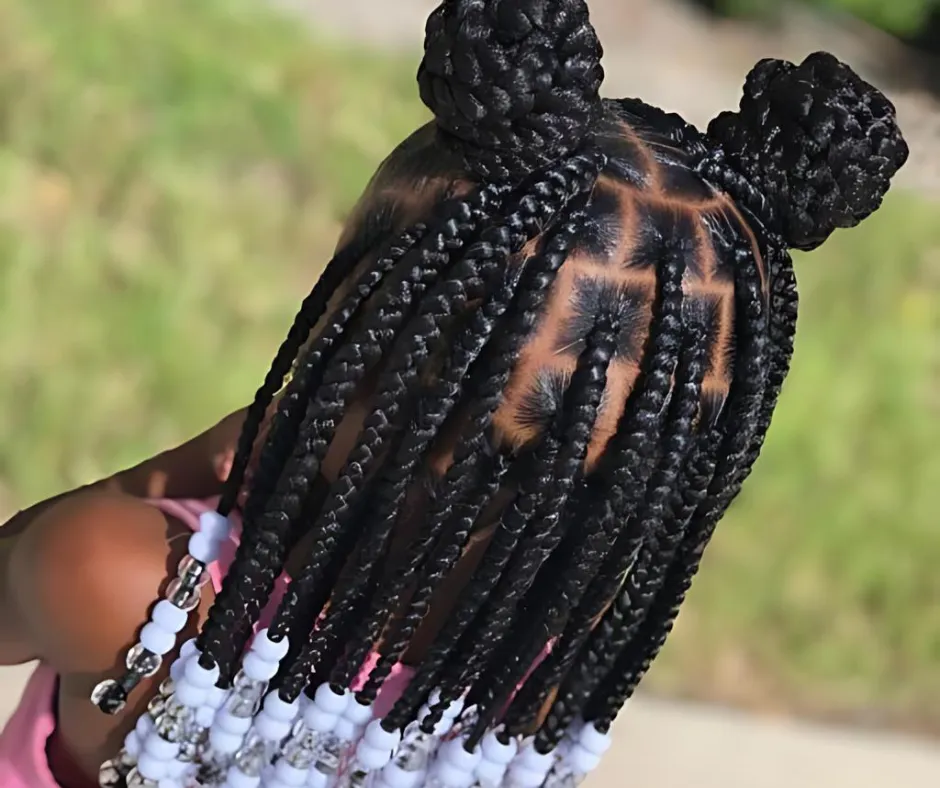 A young girl with box braids styled into two buns and decorated with white beads, viewed from the back.