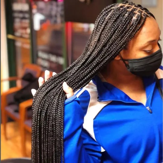 Client with long knotless braids, wearing a mask and a blue jacket, seated in Uniq Hair Braiding Salon.