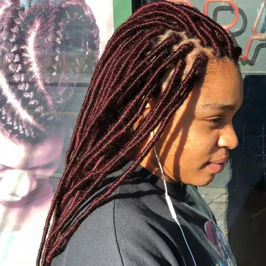 Side view of a woman with burgundy faux locs styled neatly.