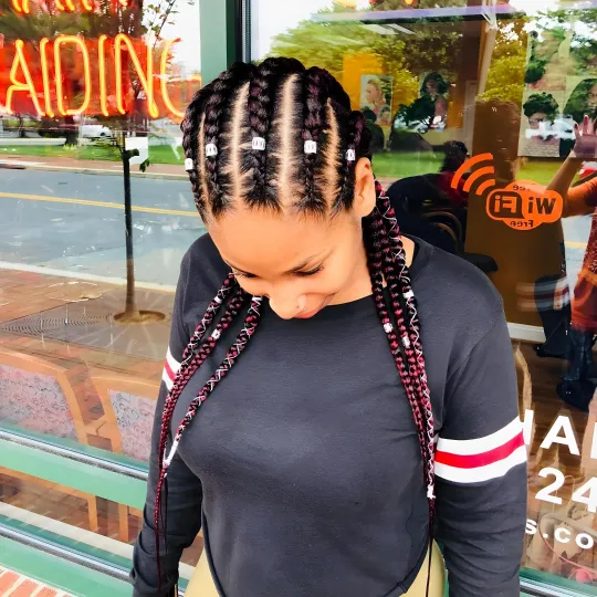 Client with cornrows braided with red extensions and beads at Uniq Braiding Salon.