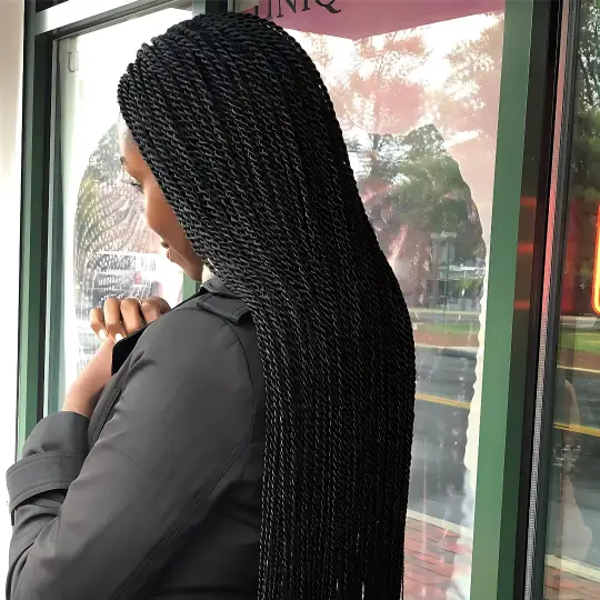 Client with long, neat Senegalese twists standing outside Uniq Hair Braiding Salon.