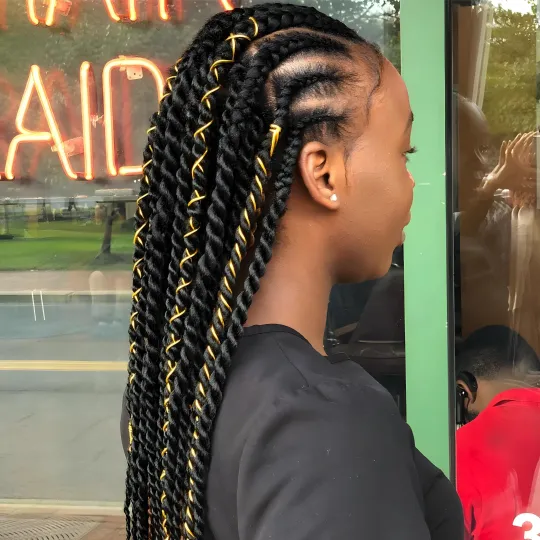Client with long Senegalese twists adorned with gold thread, standing outside Uniq Hair Braiding Salon.
