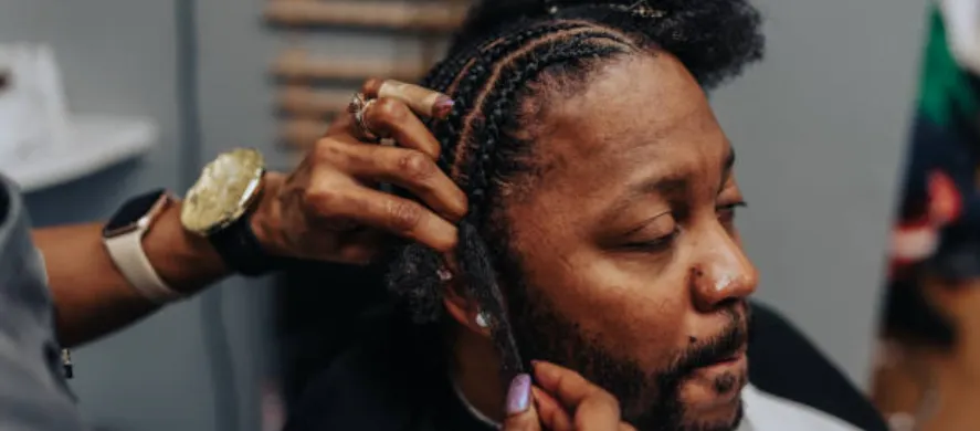 Close-up of a stylist braiding a man's hair in a unique pattern at a salon.