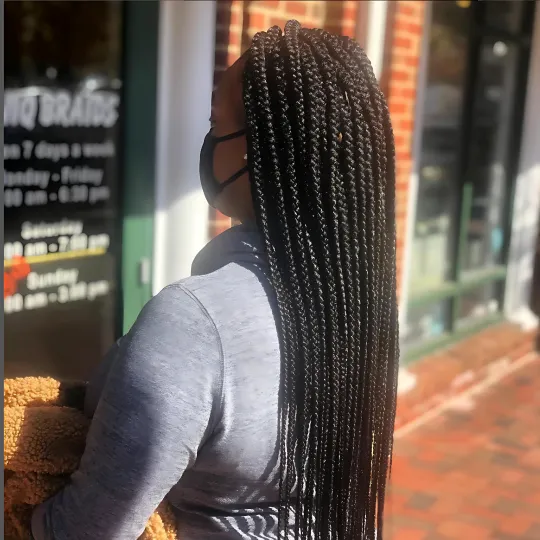 A client with long box braids standing outside Uniq Hair Braiding Salon.