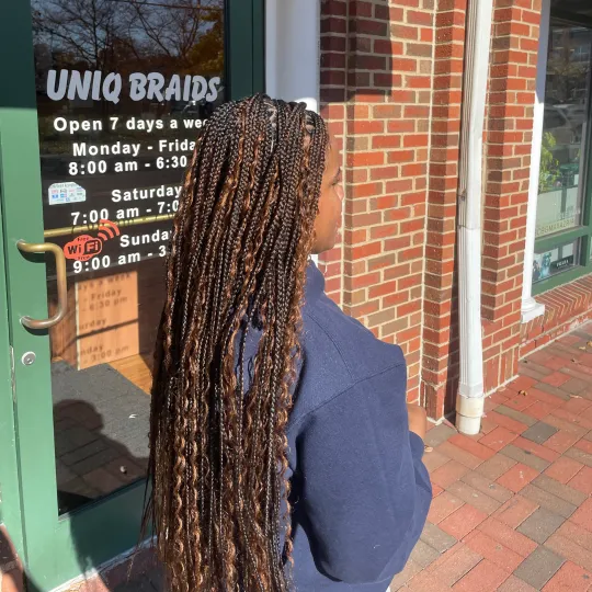 A client with long knotless braids standing outside Uniq Hair Braiding Salon.