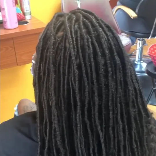 Woman with long, straight faux locs sitting in a salon chair, back view.