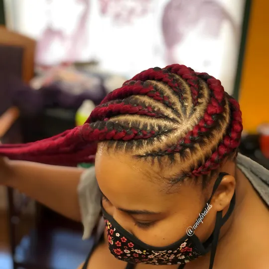 Client with red cornrows styled at Uniq Braiding Salon, wearing a mask.