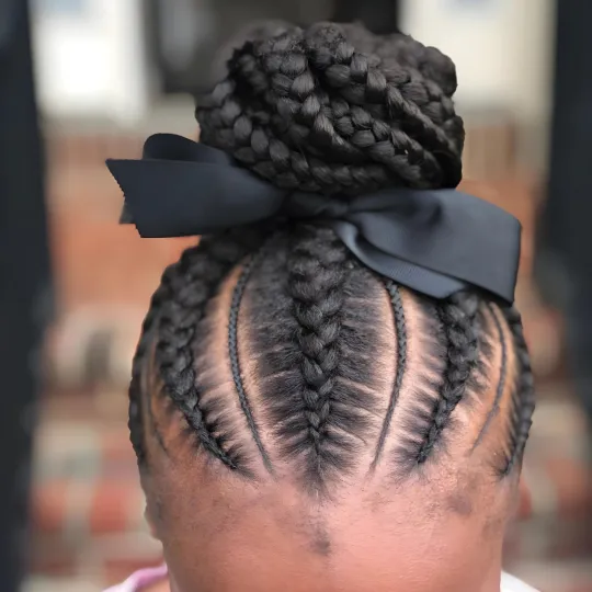 Top view of a child's braids styled into a high bun with a black ribbon.