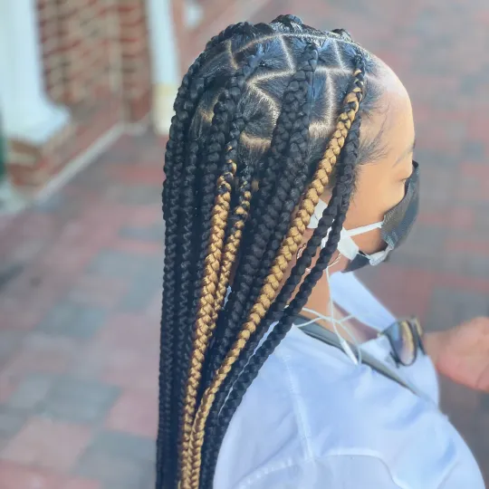 Client with black and blonde knotless braids, wearing a mask, standing outside Uniq Hair Braiding Salon.