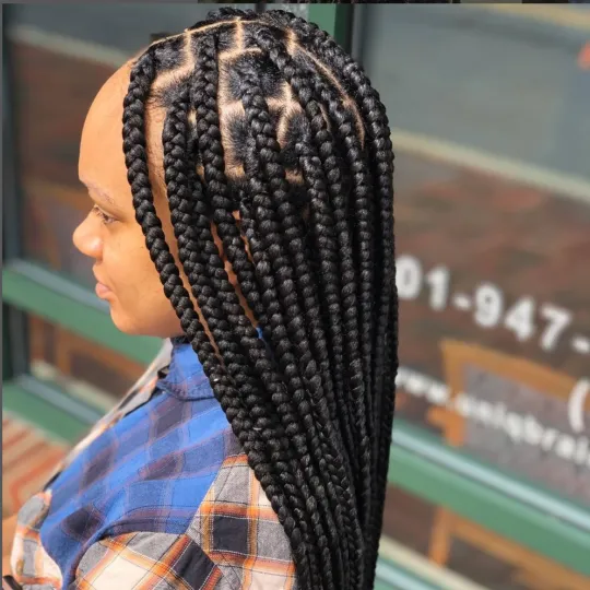 Client with long, black knotless braids standing outside Uniq Hair Braiding Salon.